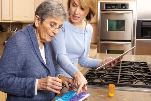 Older woman getting help with medication from female companion in kitchen.