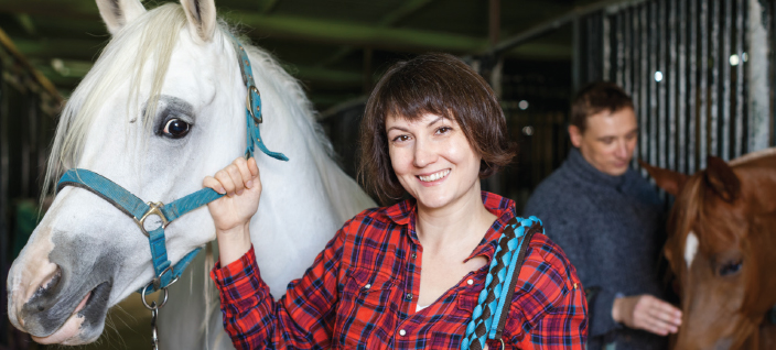 Woman smiling with white horse in barn.