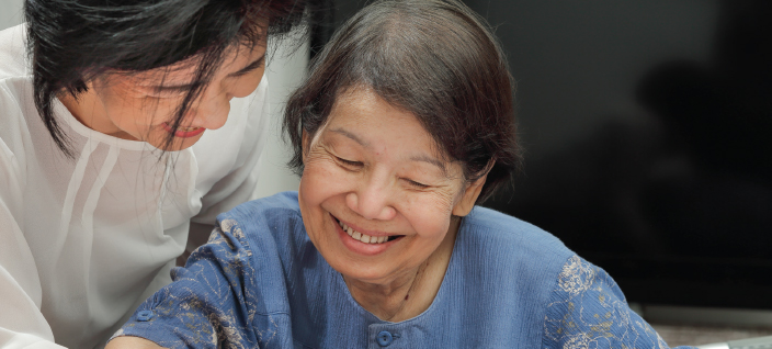 Women Reading Together Smiling, older woman reading with younger woman at her shoulder.