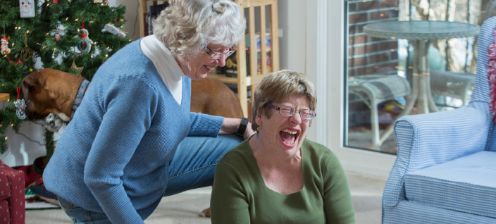 Women laughing at Christmas as one of them plays with tablet and the other watches. 