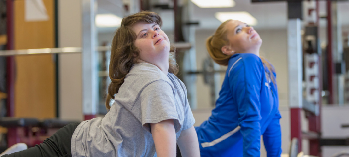Woman with down syndrome practicing yoga with another woman. 