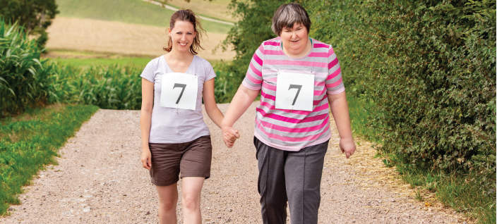 Woman walking and holding hands with support worker on gravel road in the country.