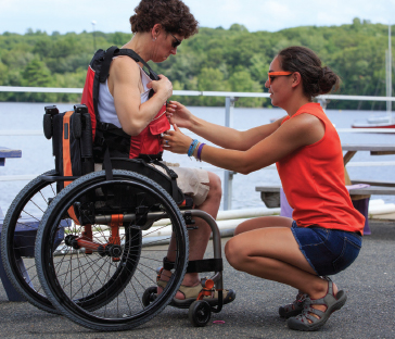 Man in wheelchair wearing life jacket being checked by woman kneeling down. 