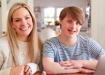 Young man with down syndrome and woman smiling at camera sitting together at home.