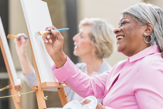 Two women smiling and painting on canvas 