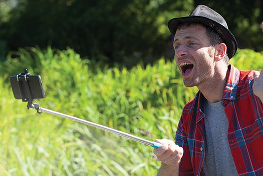 Young man in hat outside with selfie stick and camera