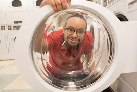 Young man with glasses looks through door of washing machine at camera